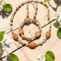 Crackling Rose Jewelry Set displayed on whitewashed wood with spring blossoms, featuring orange crackle agate ovals, yellow jade, blush pearls and clear crystals