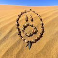 Desert Nomad Jewelry Set displayed on golden sand dunes, featuring carved tan beads, black onyx, quartz crystals and a double feather charm pendant