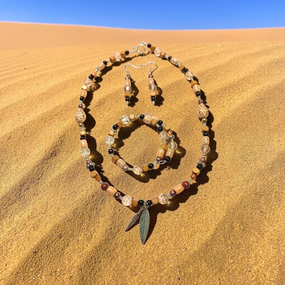 Desert Nomad Jewelry Set displayed on golden sand dunes, featuring carved tan beads, black onyx, quartz crystals and a double feather charm pendant
