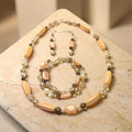 Dreaming in Pink Jewelry Set displayed on travertine stone, featuring peach mother-of-pearl ovals, smoky quartz, and freshwater pearls