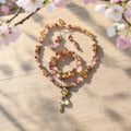 Purple Spring Jewelry Set displayed on wood with cherry blossoms, featuring pink and cranberry crystals, rose quartz, gold pendant with flower charm