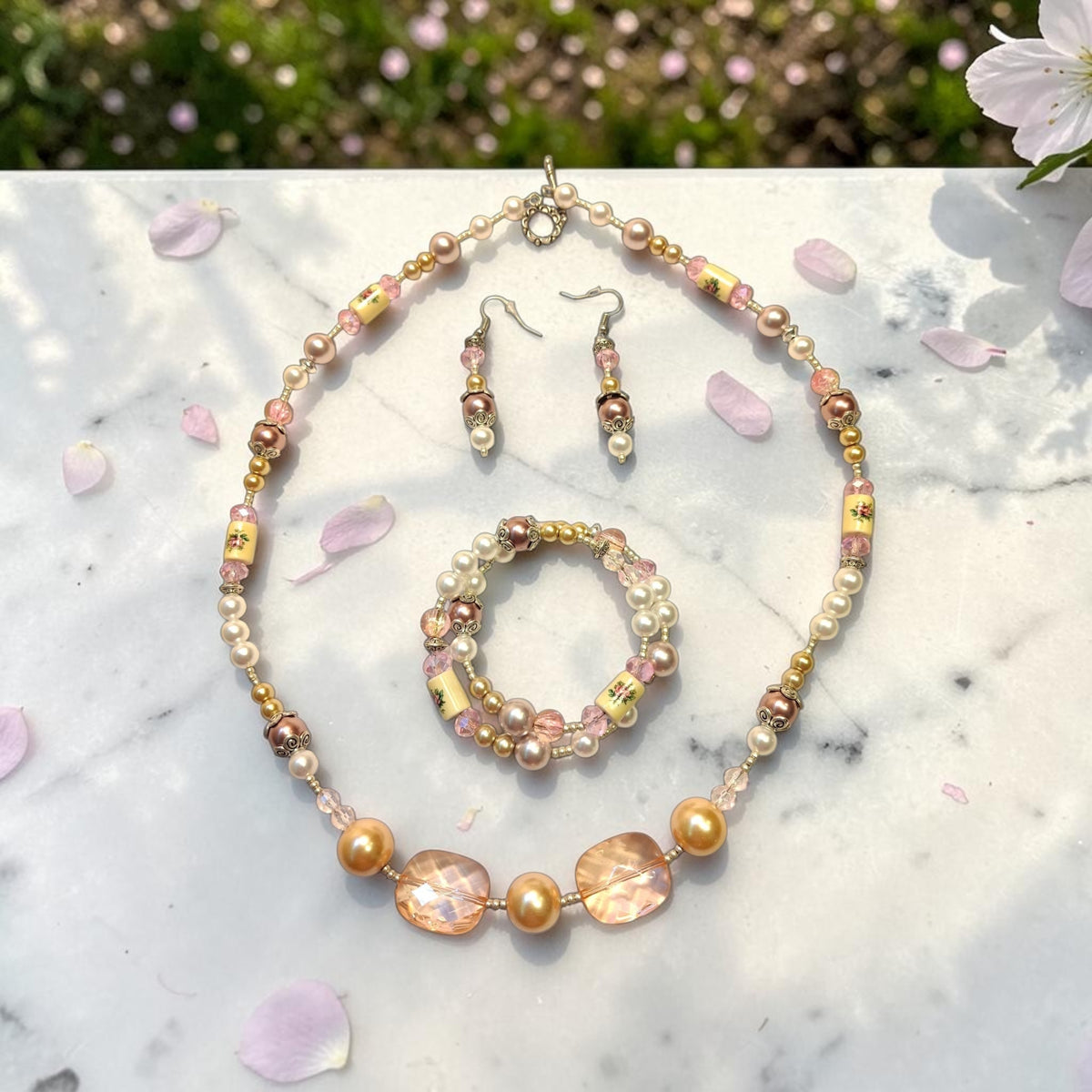 Vintage Romance Jewelry Set displayed on marble with rose petals, featuring blush pink crystals, champagne pearls, golden beads and silver filigree accents